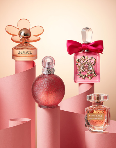 A captivating arrangement featuring four unique and beautifully shaped perfumes, artfully placed on a pink paper-like surface. This visually striking composition is skillfully photographed by David Lineton, an expert in perfume advertising photography 