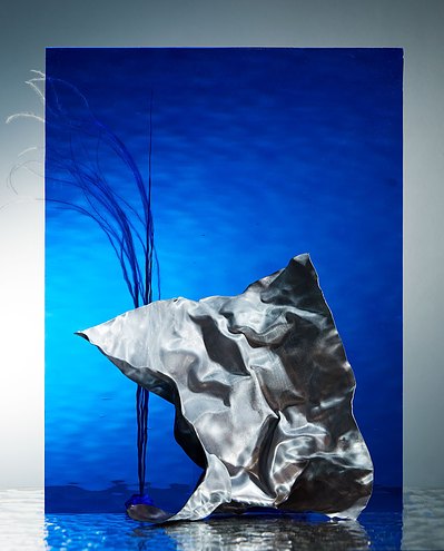 A captivating scene capturing a view of blue water with a large curtain suspended in the air just above it, influenced by fast-moving air. This stunning image is skillfully captured by David Lineton, an expert in amazing still life photography in London.