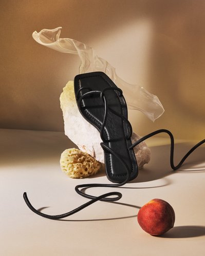 An intriguing composition showcasing shoes placed on a creamy surface with long open laces. In the foreground, an apple adds a touch of uniqueness to the image. Skillfully captured by David Lineton, an expert accessories photographer in London.
