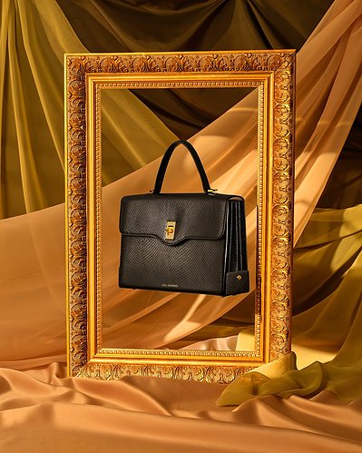 A sophisticated composition showcasing a black purse gracefully hung in the center of an empty photo frame. Skillfully captured by David Lineton, an expert accessories photographer in London