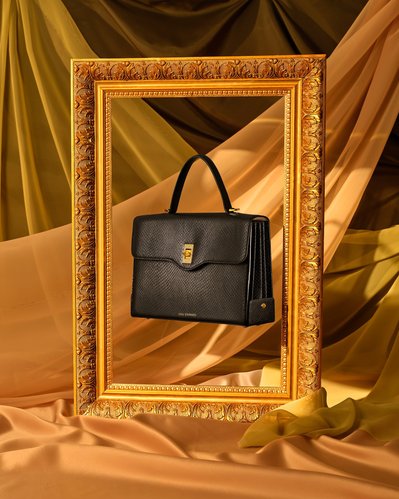 A sophisticated composition showcasing a black purse gracefully hung in the center of an empty photo frame. Skillfully captured by David Lineton, an expert accessories photographer in London