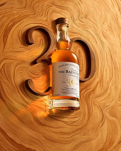A creative advertising composition featuring a drink bottle strategically placed between the numerals 3 and 0 on a wooden surface. Skillfully photographed by David Lineton, an expert drinks advertising photographer in London