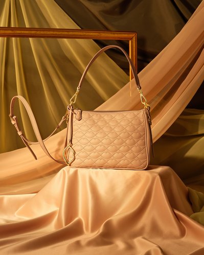 A sophisticated composition featuring a light brown handbag placed on a surface with the same-colored curtain. Expertly captured by David Lineton, an experienced accessories photographer in London