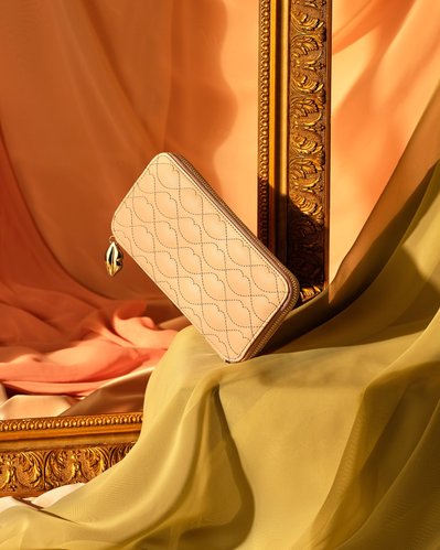 An elegant composition featuring a purse artfully balanced on a surface in front of an empty golden photo frame. Skillfully captured by David Lineton, an expert in accessories photography in London