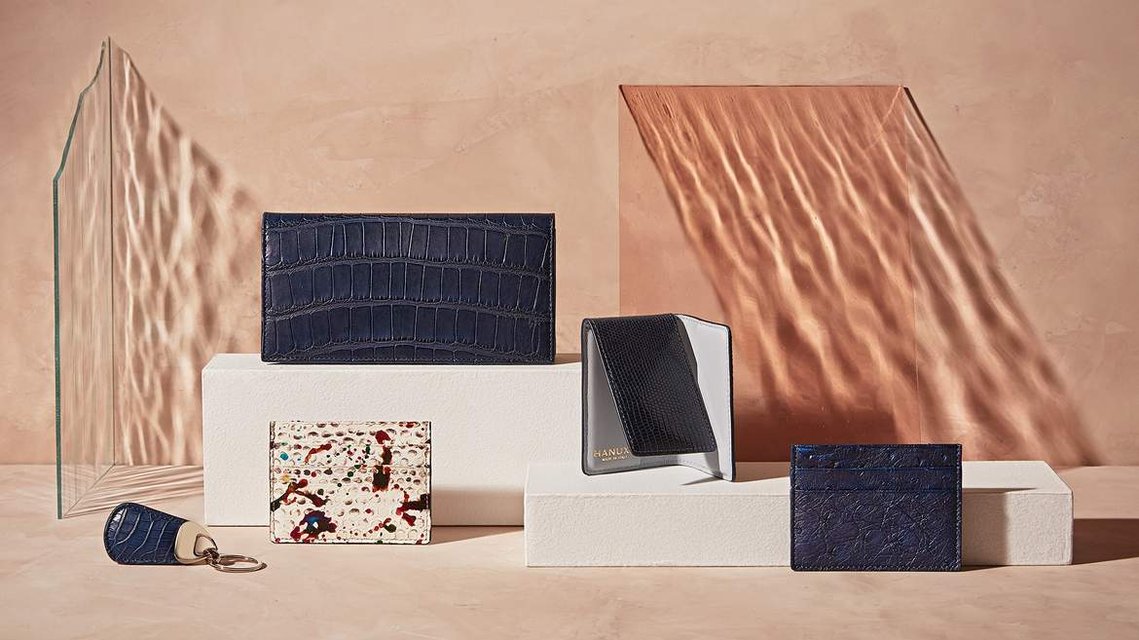 Hanuxe Leather accessories, wallets, purses and keyring, sitting on top of some textural plinths with coloured refracted light cascading across the image