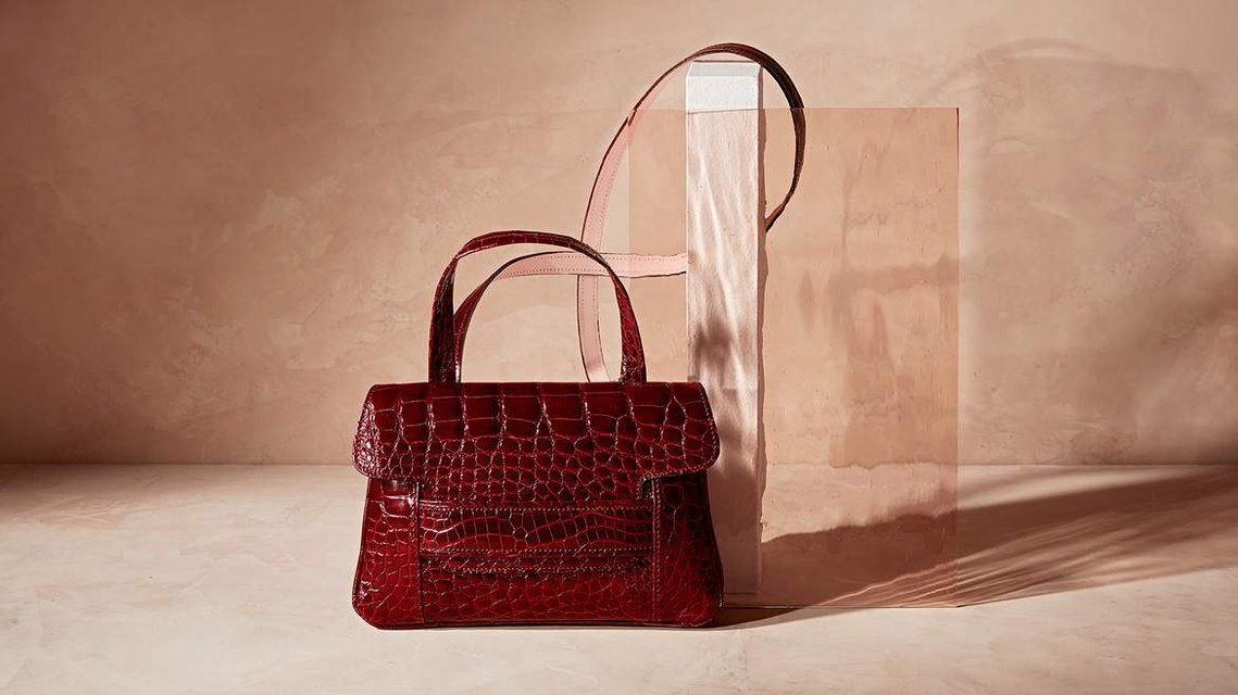 a graphic red and striking leather handbag, the strap is intertwined through the set with a shaft of coloured art glass offering a smoothness to the scene.