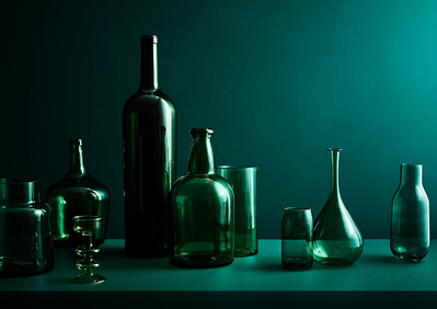 A striking composition featuring multiple green bottles and glasses artfully arranged on a green table against a green background. This skillfully captured photograph is the work of David Lineton, an expert creative product photographer in London.