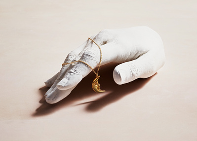 A minimalist and artistic composition featuring a necklace delicately placed on the fingers of a cut white hand. This visually striking image is skillfully photographed by David Lineton, an expert in commercial jewelry photography in London.