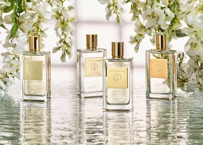 A serene composition capturing four perfume bottles gracefully placed on a water-like surface, surrounded by delicate white flowers. This tranquil scene is skillfully photographed by David Lineton, an expert in perfume photography in London