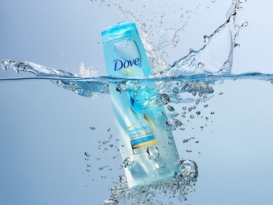 An evocative scene capturing Dove shampoo, seemingly fallen into water with scattered droplets creating a dynamic and refreshing composition, skillfully photographed by David Lineton, an expert still-life photographer in London