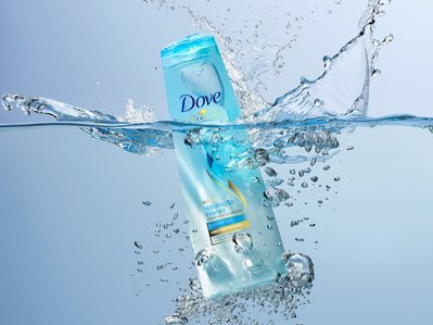 An evocative scene capturing Dove shampoo, seemingly fallen into water with scattered droplets creating a dynamic and refreshing composition, skillfully photographed by David Lineton, an expert still-life photographer in London