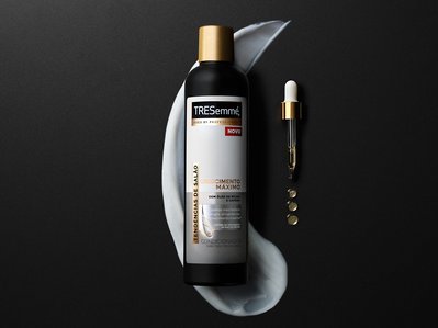 A captivating advertisement showcasing Tresemme conditioner elegantly positioned on a sleek black surface. The surrounding area, predominantly black, provides a striking contrast to the specific spot beneath the conditioner. 