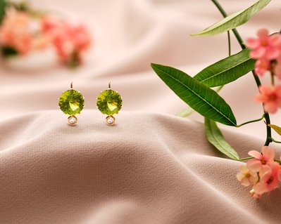 A harmonious composition featuring two green-colored earrings placed on a surface alongside green leaves and flowers. This visually appealing arrangement is skillfully photographed by David Lineton, an expert in professional jewelry photography.