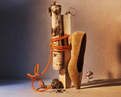 A creatively composed image featuring a smooth wood block intricately tied with a rough block of wood, with a vertically placed shoe, expertly captured by David Lineton, a seasoned accessories photographer in London.