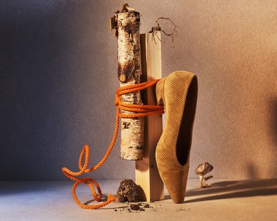 A creatively composed image featuring a smooth wood block intricately tied with a rough block of wood, with a vertically placed shoe, expertly captured by David Lineton, a seasoned accessories photographer in London.