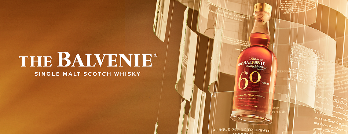 The Balvenie 60 Years single-casked Malt whiskey. Paines of glass with etching of quotes surrounds the hero bottle. A warm wash of honey glow lighting enhances the tones and colour of the whiskey bottle