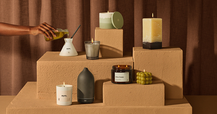 A rich, brown and tan stepped set with a brown pleated curtain greats depth against the home fragrance candles that are lit and sitting on the four levels of the stone and rough surface plinths 