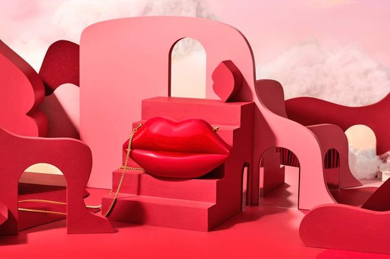 The Red Lulu Guinness Lip Clutch bag sits on a red staircase set with abstract lip forms creating leading lines across the images. Whispy cloudscapes make the image feel like it is in cloud 9