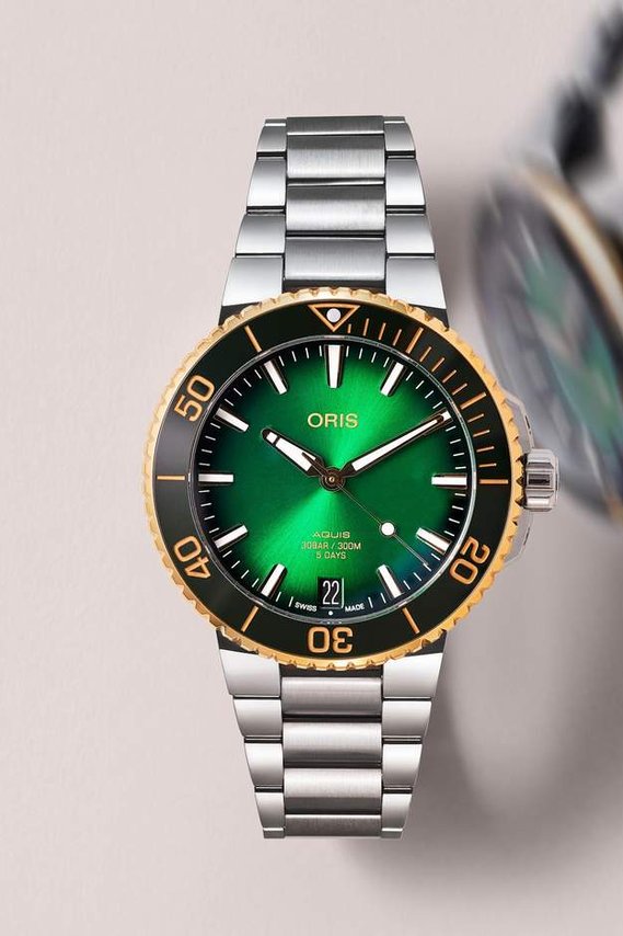 Oris Stainless Steel Watch with a black and Rich green dial with gold details Framed with a contact shadow and motion blur watch in the background.