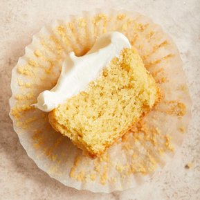 Half of a vanilla cupcake with cream cheese frosting on a cupcake wrapper.
