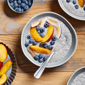 Chia pudding in a blue bowl with blueberries and nectarine slices on top.