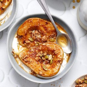 Two baked pear halves in a bowl with yogurt and granola and a spoon in the bowl.