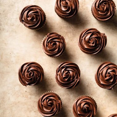 Frosted chocolate cupcakes arranged on a beige surface.