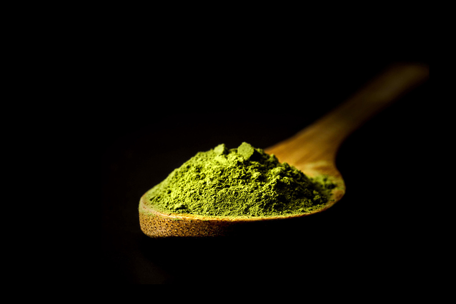 dramatically lit bamboo spoon of matcha tea on a black background