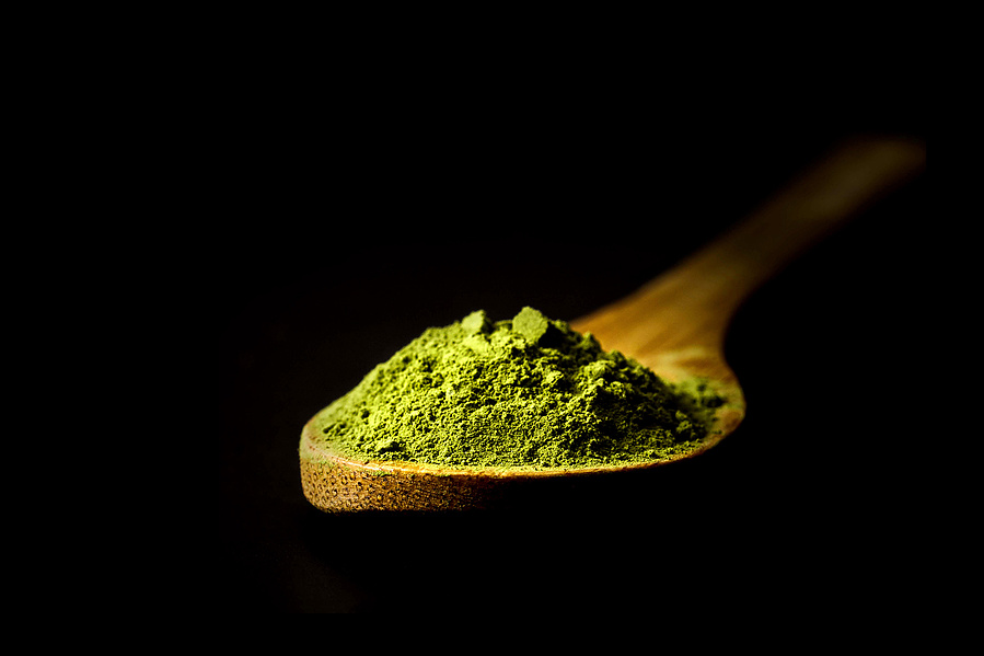 dramatically lit bamboo spoon of matcha tea on a black background