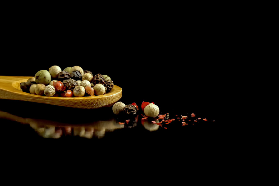 colorful peppercorns on a tiny bamboo spoon on a black background with a reflection
