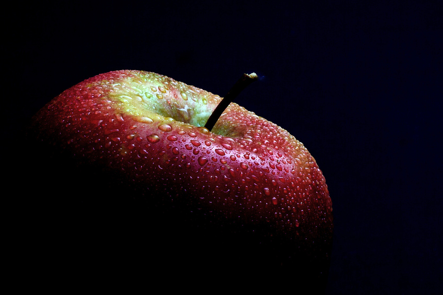 Apple covered in dew drops on a dramatic black background.
