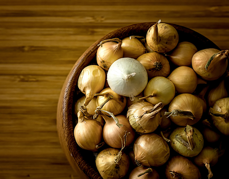 small wooden bowl of yellow pearl onions with one white pearl onion