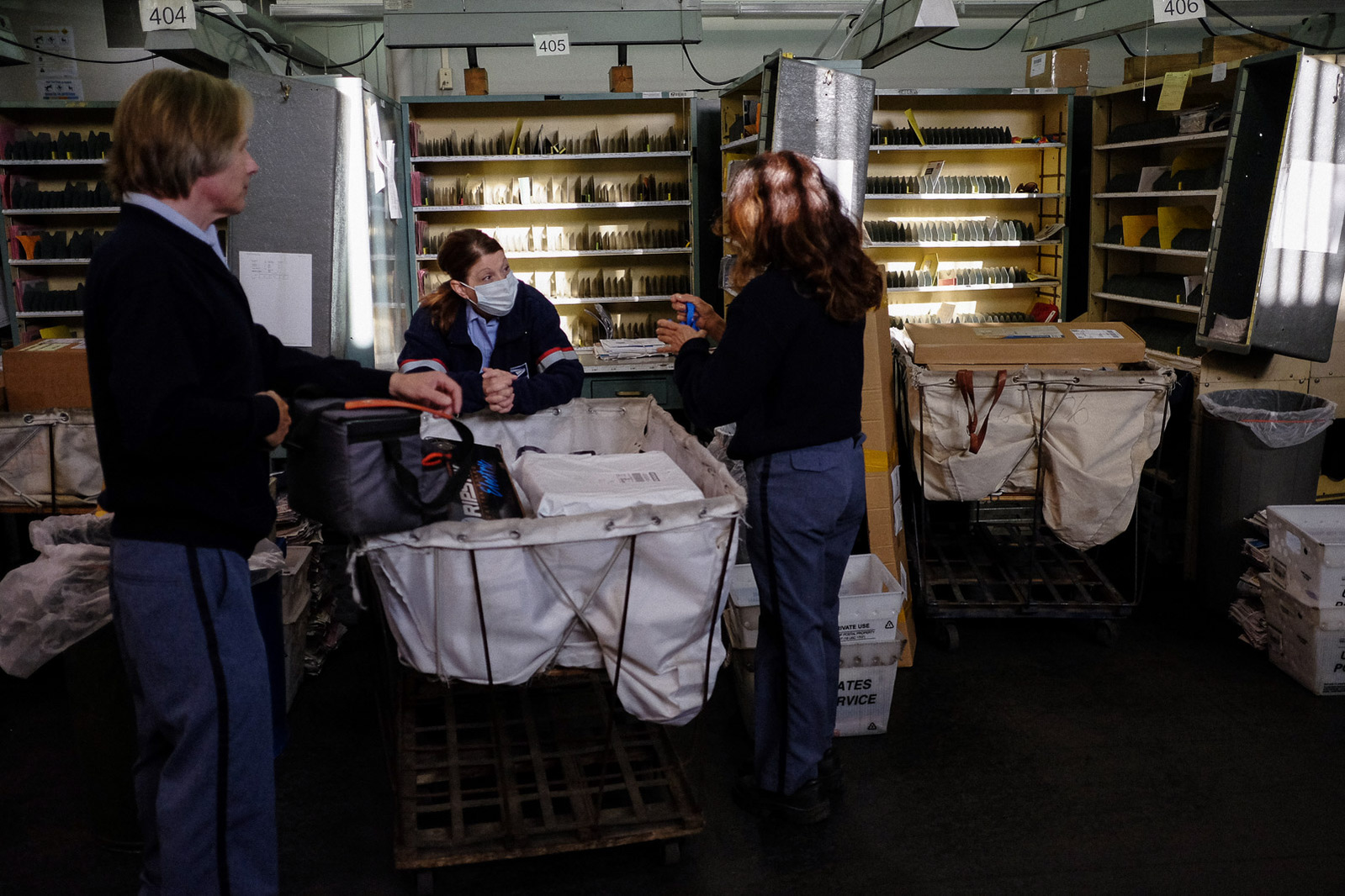 Letter Carriers Ray and Deb Reid and Tammy Sheahan (left to right) chat before sorting mail for their routes at the USPS’s Boardwalk branch on Tuesday, May 5, 2020 in Saginaw Township, Mich.