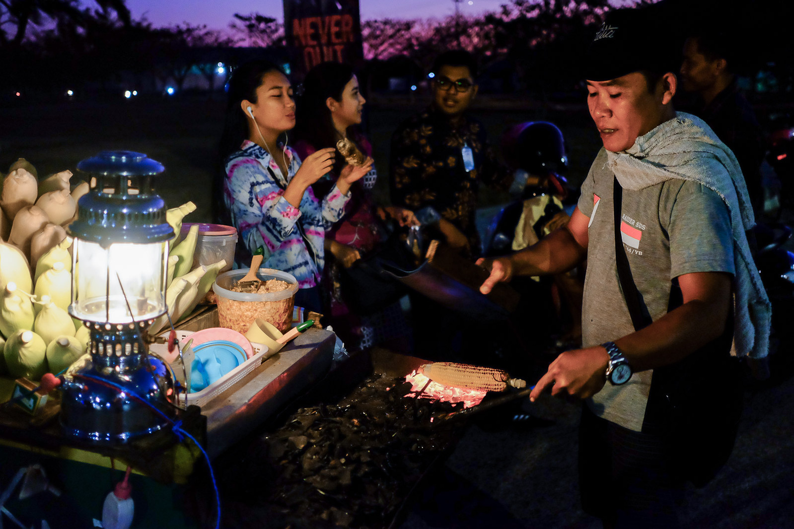 Om Saldi (right) grills corn for customers by the side of busy thoroughfare on September 13, 2019 in Kupang, Indonesia.
