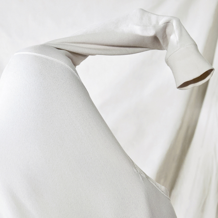 Close up of a figure hiding inside a white pullover, the sleeve overhead up in the air in front of a white curtain
