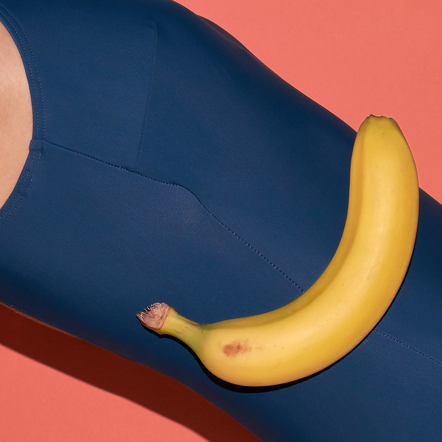 Detail of a petrol colored bathing suit with a yellow banana in front and an apricot colored background
