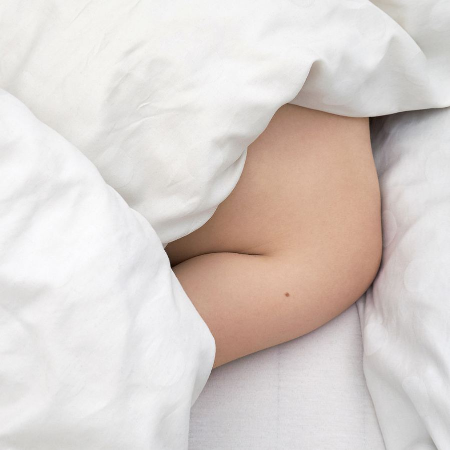 Close up of the naked shoulder of a woman hiding under crinkled white bad sheets