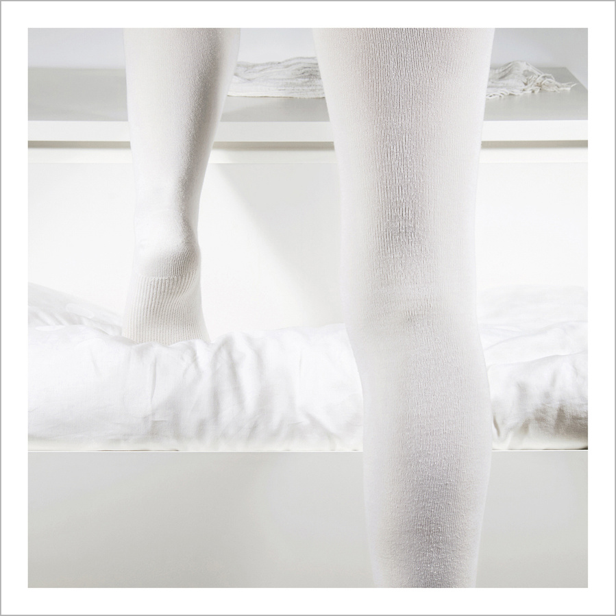 Backside of a woman's legs wearing white tights stepping up a white drawer filled with white bedsheets