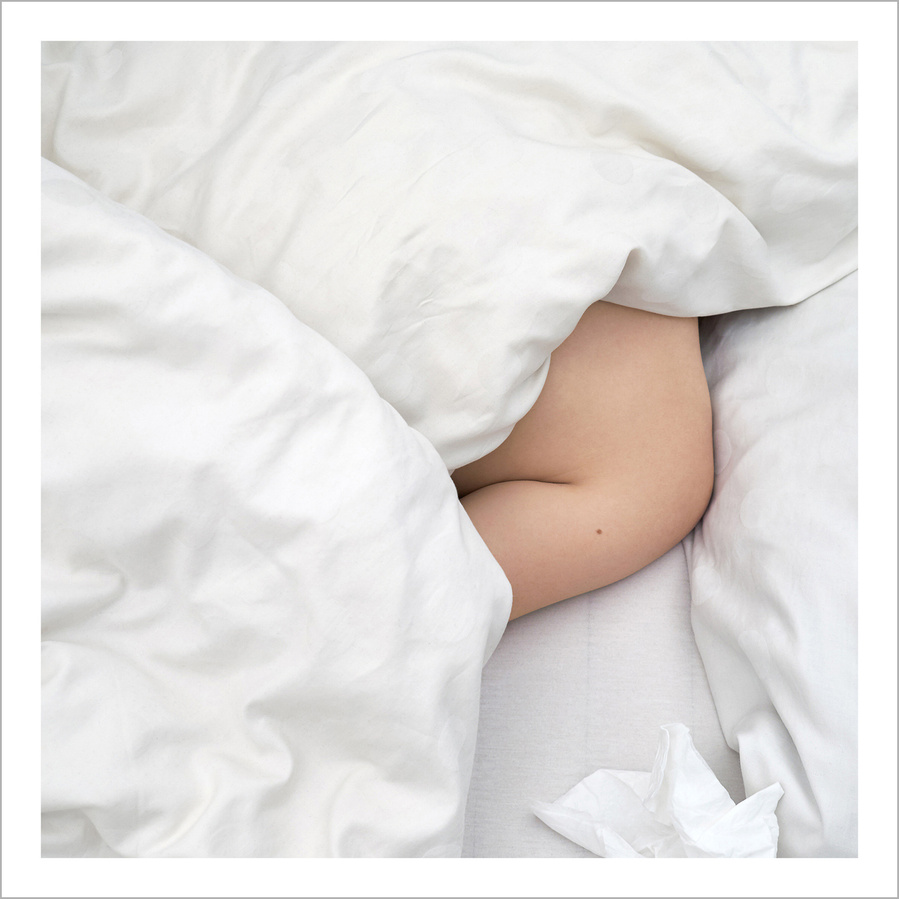 The naked shoulder of a woman hiding under crinkled white bad sheets with crinkled white tissues next to her