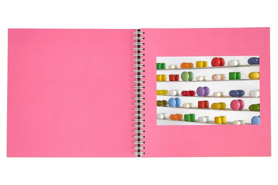 An open book with pink colored pages showing the photograph of colorful pills in a mirror cabinet