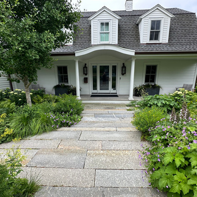 Reclaimed granite paths lead to a lush entry garden of Acanthus, Geranium, Sesleria, and hydrangea, balancing structure and softness.