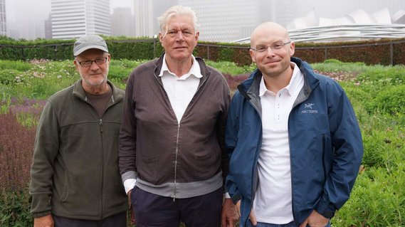 Roy Diblik, Piet Oudolf, and Adam Woodruff standing together at Lurie Garden in Chicago, surrounded by lush, naturalistic planting with the city skyline in the background.