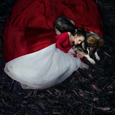 A person in a red dress and a dog laying together in the woods.