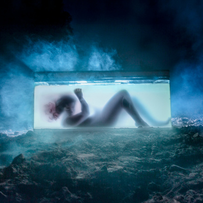 Photographic art of a silhouetted person in a glass box,  surrounded by haze.