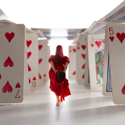 Photographic Art of A person in a red dress walking through a room with playing cards.