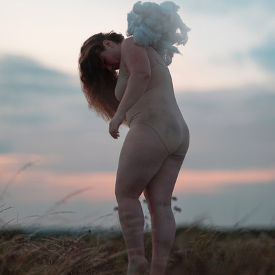 A person in a nude coloured garment with clouds on her back, pulling her up.
