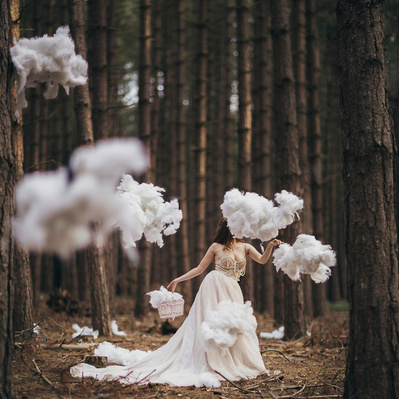 Photographic art of A person in a white dress in the woods surrounded by floating clouds.