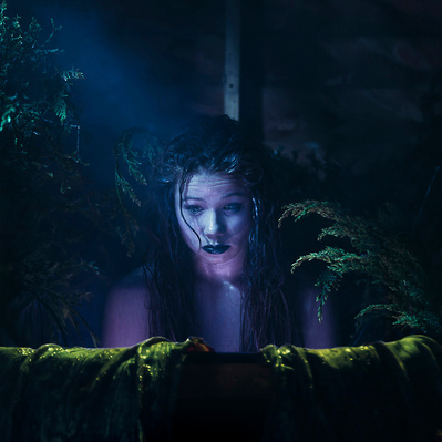 Photographic art of a mermaid character in a dark outside environment.