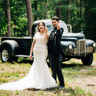 A newlywed couple flicking off the camera with a classic truck behind them.