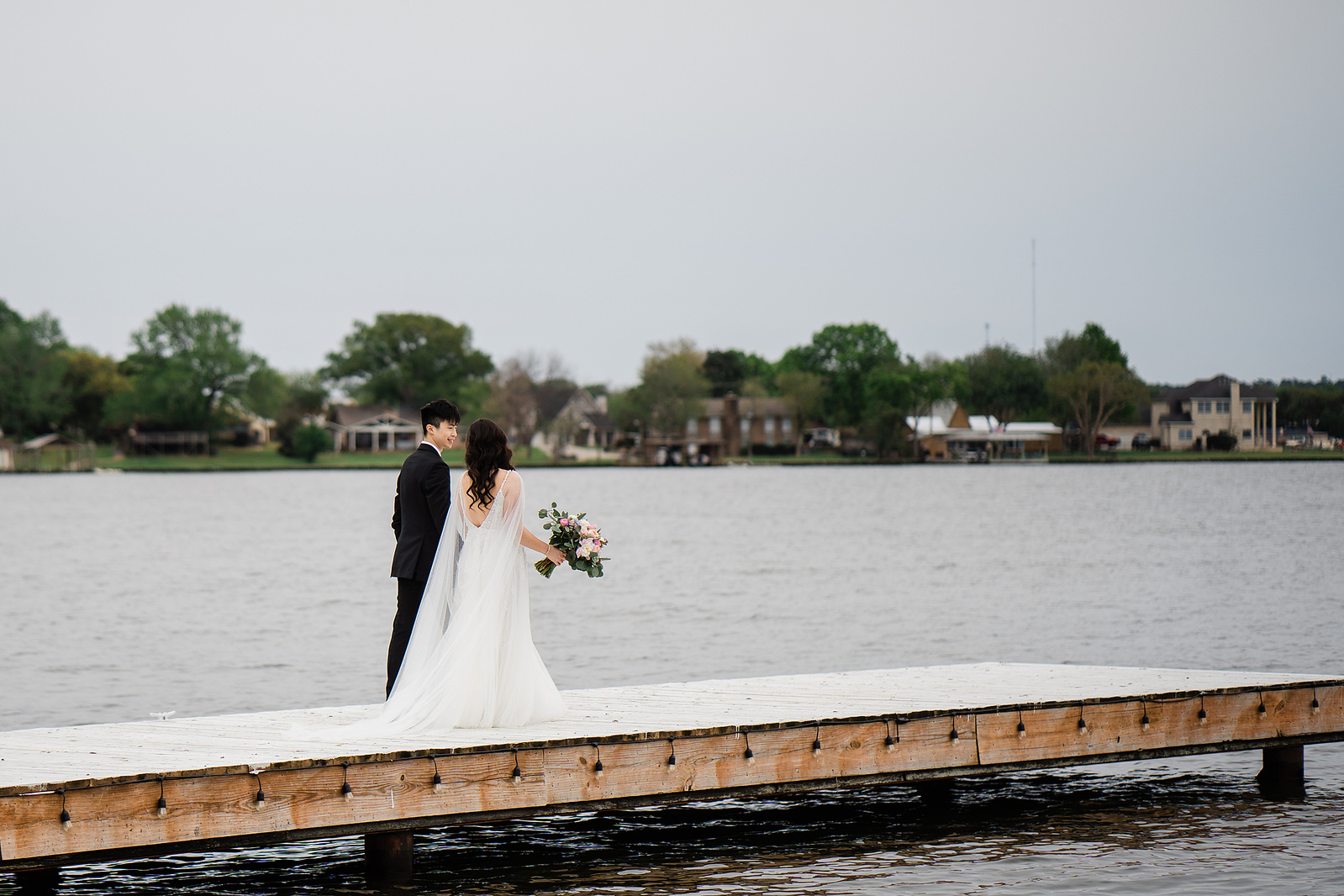 A bride and groom walking together towards a lake.